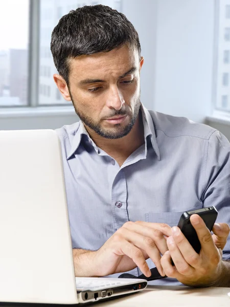 Homme d'affaires travaillant sur ordinateur portable en utilisant le téléphone mobile au bureau devant la fenêtre du gratte-ciel — Photo