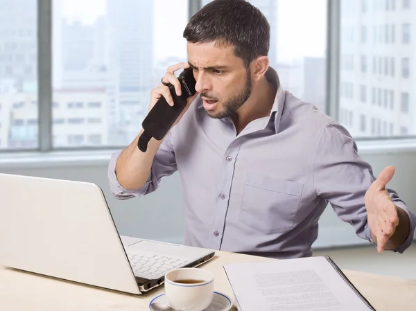 Homme d'affaires au bureau devant gratte-ciel vue fenêtre parler bouleversé sur le téléphone de travail avec l'ordinateur — Photo