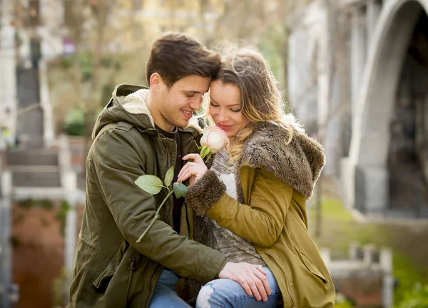 Pareja con rosa en el amor besándose en callejón celebrando San Valentín con pasión sentado en el parque de la ciudad — Foto de Stock