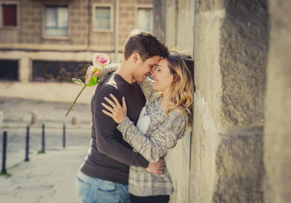 Candid portrait of beautiful European couple with rose in love kissing on street alley celebrating Valentines day — Stock Photo, Image