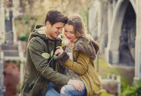 Pareja con rosa en el amor besándose en callejón celebrando San Valentín con pasión sentado en el parque de la ciudad — Foto de Stock