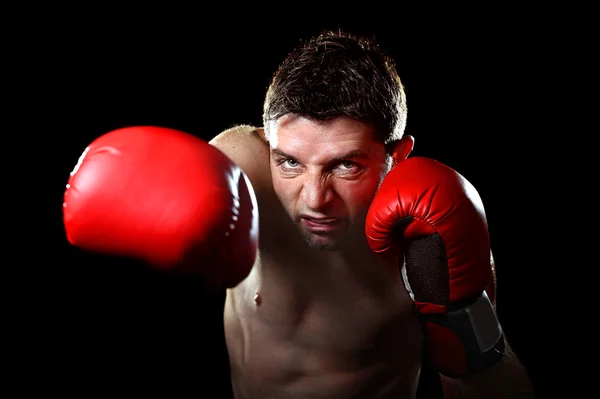 Agresivo luchador hombre entrenamiento sombra boxeo con guantes de combate rojo lanzando golpe derecho vicioso —  Fotos de Stock