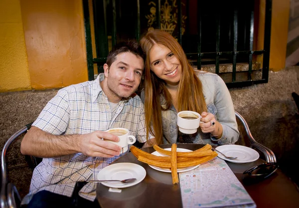 Jovem belo casal turista americano tendo espanhol café da manhã típico chocolate quente com churros sorrindo feliz — Fotografia de Stock