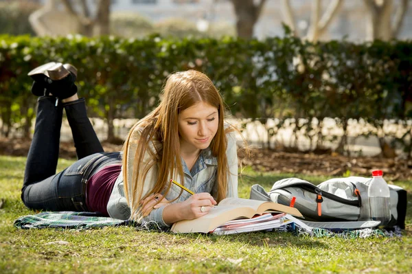 young beautiful student girl on campus park grass with books studying happy preparing exam in education concept