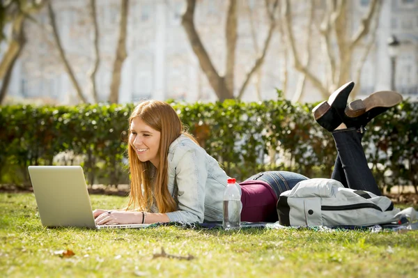 Young student girl lying on park grass with computer studying or surfing on internet — Stock Photo, Image