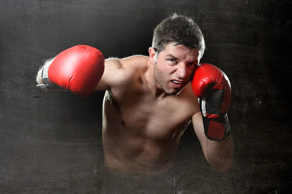 Hombre furioso entrenamiento de boxeo en el gimnasio con guantes de combate rojos lanzando golpe vicioso — Foto de Stock