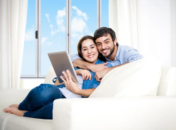 Joven pareja feliz en el sofá en casa disfrutando con la tableta digital —  Fotos de Stock