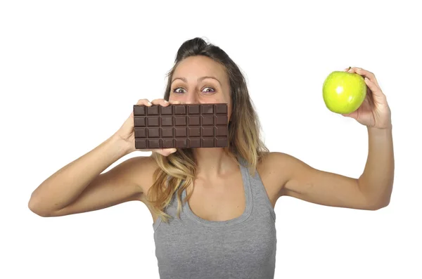 Attractive woman holding apple and chocolate bar in healthy fruit versus sweet junk food temptation — Stock Photo, Image