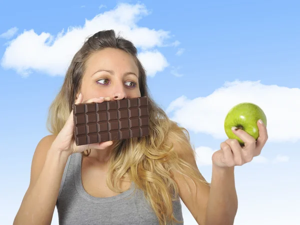 Attractive woman holding apple and chocolate bar in healthy fruit versus sweet junk food temptation — Stock Photo, Image