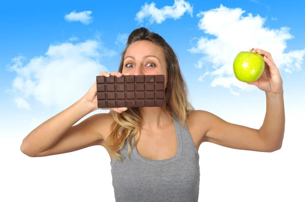 Atractiva mujer sosteniendo barra de manzana y chocolate en fruta sana versus comida chatarra dulce tentación — Foto de Stock