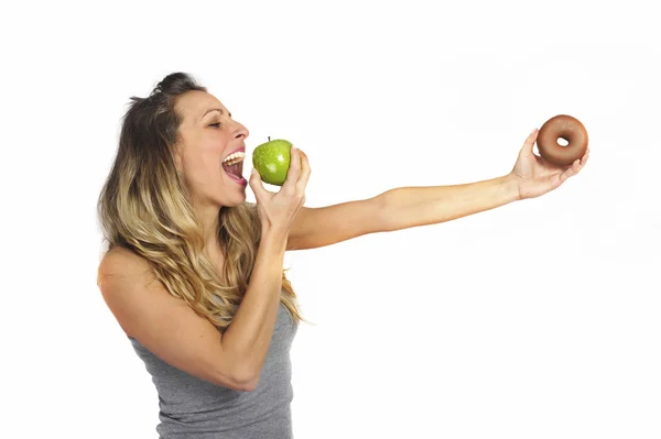 Mulher atraente segurando maçã e donut de chocolate em frutas saudáveis versus doce junk food tentação — Fotografia de Stock