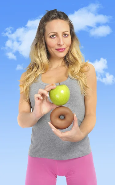 Attractive woman holding apple and chocolate donut in healthy fruit versus sweet junk food temptation — Stock Photo, Image