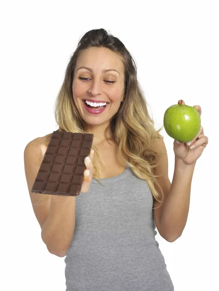 Attraktiv kvinna med äpple och choklad bar i hälsosamma frukt kontra söt skräpmat frestelsen — Stockfoto