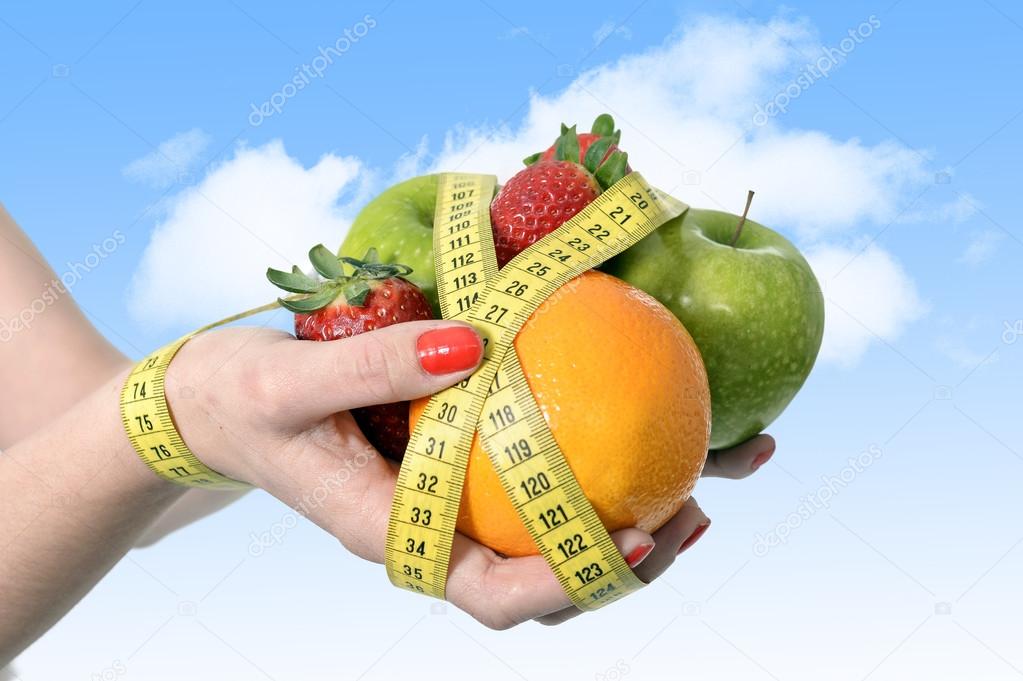 Woman hands with mix of fruit bond wrist wrapped with measure tape in dieting