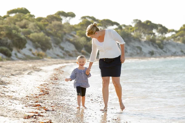 Mãe feliz segurando mão de doce loira pequena filha andando juntos na areia na praia costa do mar — Fotografia de Stock