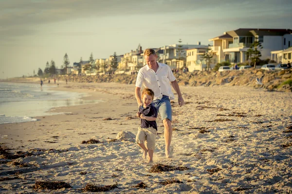 Happy father playing on the beach with little son running excited with barefoot in sand and water — Stock Photo, Image