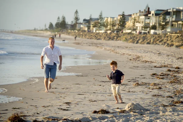 Ayah yang bahagia bermain di pantai dengan anak kecil berlari gembira dengan bertelanjang kaki di pasir dan air — Stok Foto