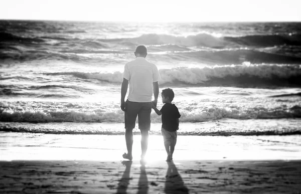 Pai feliz segurando a mão do pequeno filho andando juntos na praia com os pés descalços — Fotografia de Stock