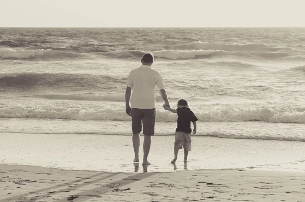 Happy father holding holding hand of little son walking together on the beach with barefoot — Stock Photo, Image