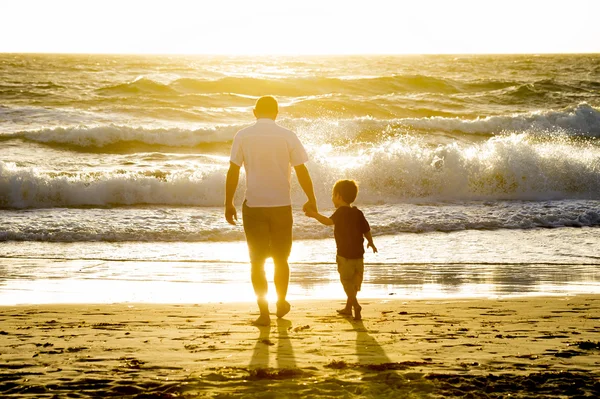 Pai feliz segurando a mão do pequeno filho andando juntos na praia com os pés descalços — Fotografia de Stock