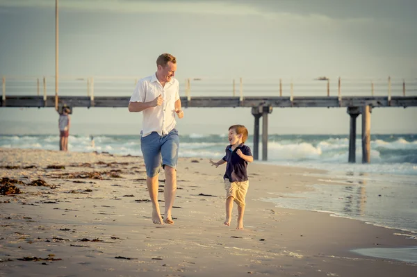 Happy father playing on the beach with little son running excited with barefoot in sand and water — Stock Photo, Image