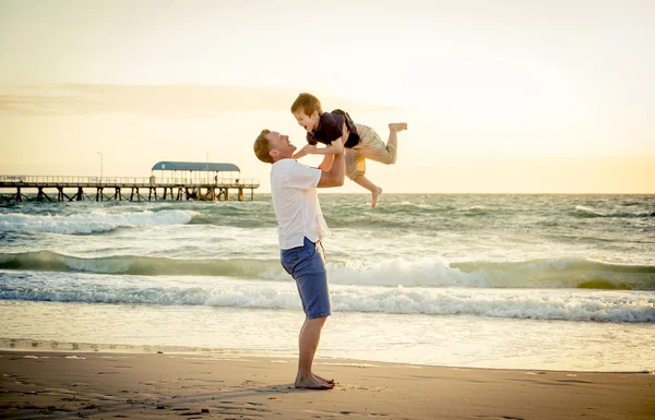 Młody szczęśliwy ojciec trzyma się w jego ramiona mały syn stawiania go na plaży — Zdjęcie stockowe