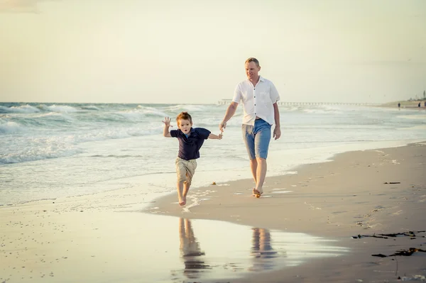 Feliz padre jugando en la playa con su pequeño hijo corriendo excitado con los pies descalzos en la arena y el agua — Foto de Stock