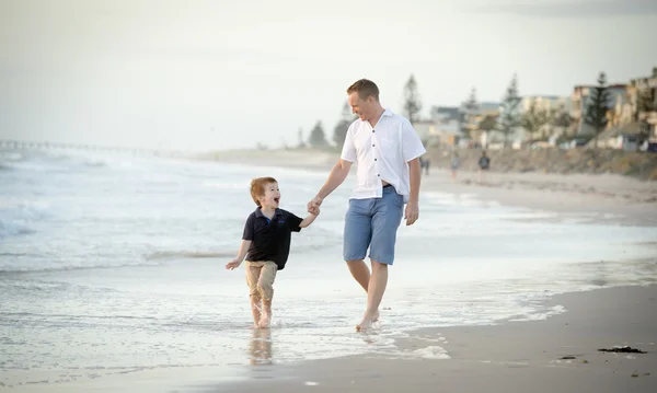 Happy father holding holding hand of little son walking together on the beach with barefoot — Stock Photo, Image