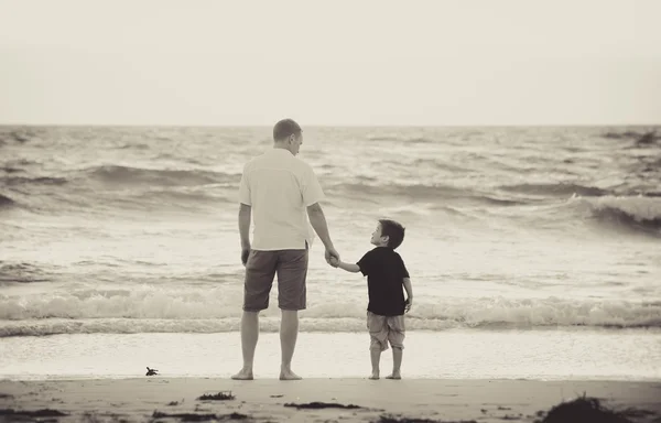 Pai feliz segurando a mão do pequeno filho andando juntos na praia com os pés descalços — Fotografia de Stock