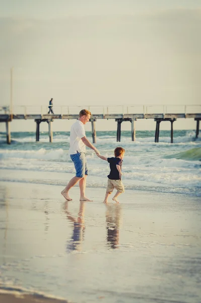 Gelukkig vader spelen op het strand met zoontje uitgevoerd enthousiast met blote voeten in het zand en water — Stockfoto