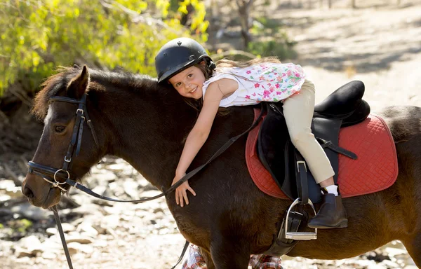 Doce jovem menina abraçando pônei cavalo sorrindo feliz vestindo capacete de segurança jockey em férias de verão — Fotografia de Stock