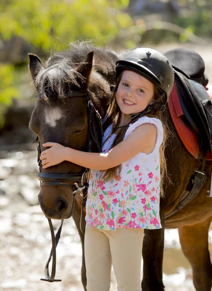 Douce belle jeune fille 7 ou 8 ans étreignant la tête de petit cheval de poney souriant heureux portant un casque de jockey de sécurité pendant les vacances d'été — Photo