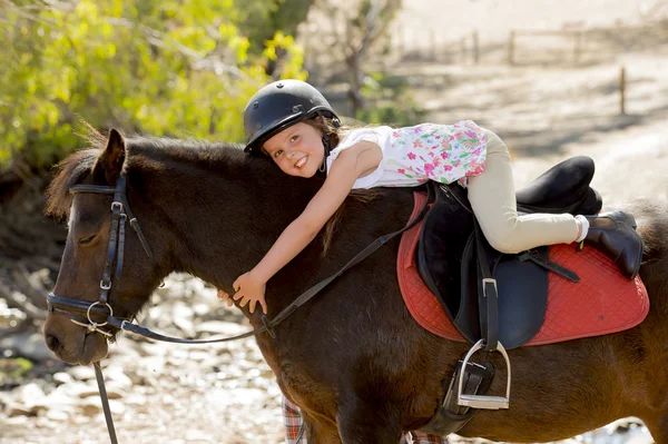 sweet young girl hugging pony horse smiling happy wearing safety jockey helmet in summer holiday