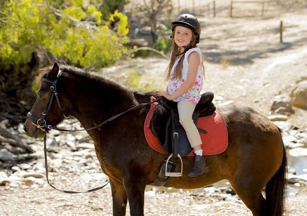 Γλυκιά κοπέλα 7 ή 8 ετών ιππασίας πόνι άλογο χαμογελαστό ευτυχισμένη φορώντας jockey κράνους ασφαλείας σε καλοκαιρινές διακοπές — Φωτογραφία Αρχείου