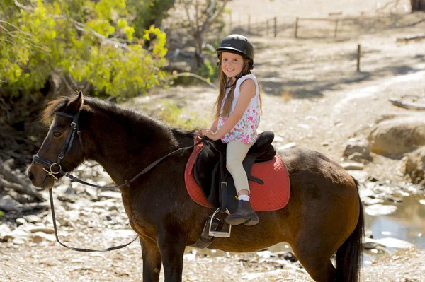 Γλυκιά κοπέλα 7 ή 8 ετών ιππασίας πόνι άλογο χαμογελαστό ευτυχισμένη φορώντας jockey κράνους ασφαλείας σε καλοκαιρινές διακοπές — Φωτογραφία Αρχείου