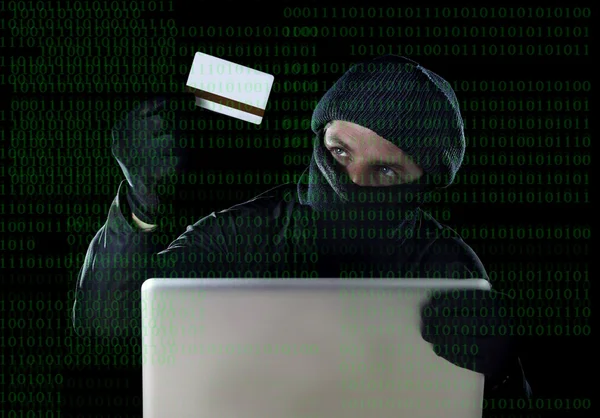 Man in black holding credit card using computer laptop for criminal activity hacking password and private information — Stock Photo, Image