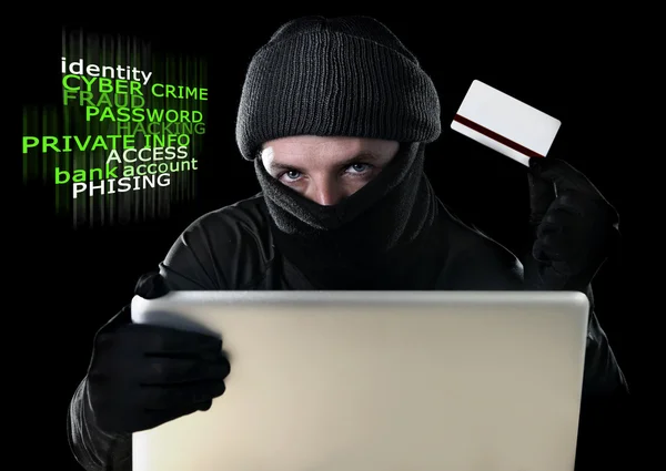 Mannen i svart anläggning kreditkort med hjälp av dator laptop för brottslig verksamhet hacking lösenord och privat information — Stockfoto