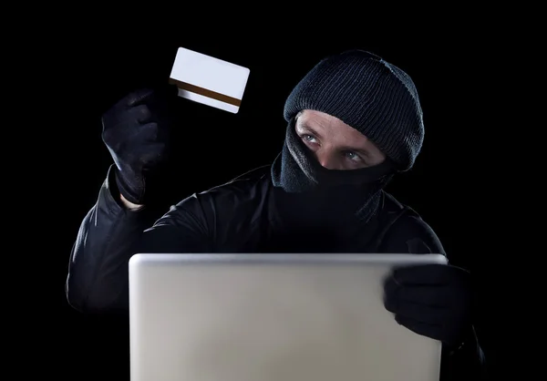 Mężczyzna w czarnym gospodarstwa karta kredytowa przy pomocy komputera laptop do działalności przestępczej, hackowanie hasła i prywatny informacja — Zdjęcie stockowe