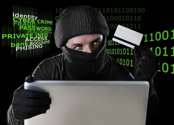 Homem em preto segurando cartão de crédito usando laptop computador para a atividade criminosa hacking senha e informações privadas — Fotografia de Stock