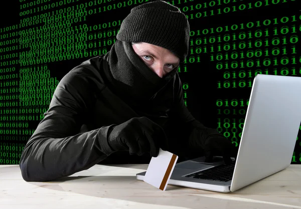 Man in black holding credit card using computer laptop for criminal activity hacking password and private information — Stock Photo, Image