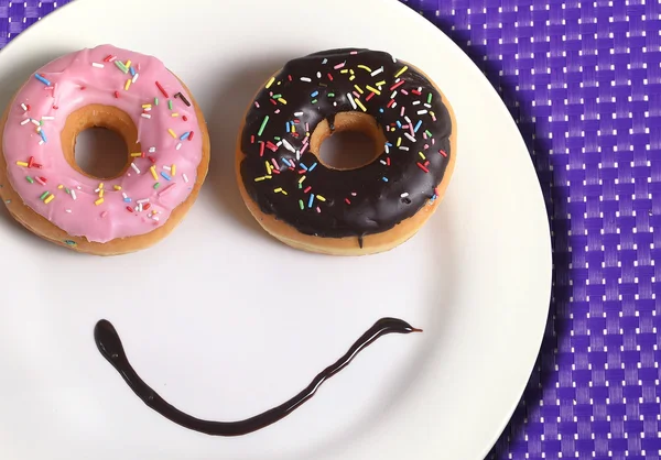 smiley happy face made on dish with donuts eyes and chocolate syrup as smile in sugar and sweet addiction nutrition