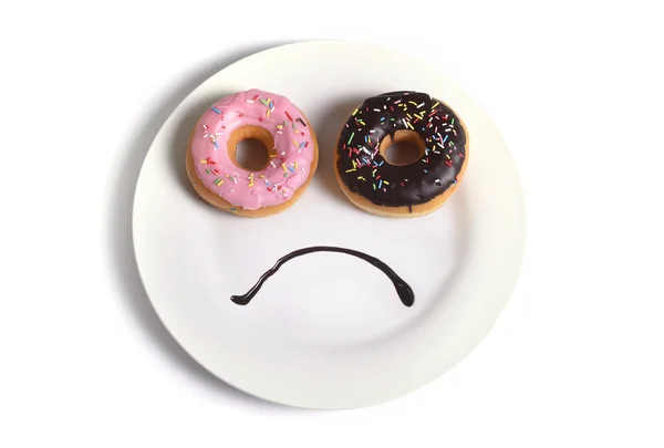 Rosto triste sorridente feito no prato com donuts como olhos e boca de xarope de chocolate em açúcar dieta de vício doce e nutrição — Fotografia de Stock