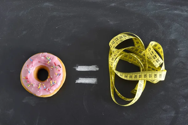 Donut e alfaiate fita métrica no quadro negro em açúcar doce abuso e dependência corpo igual excesso de peso — Fotografia de Stock