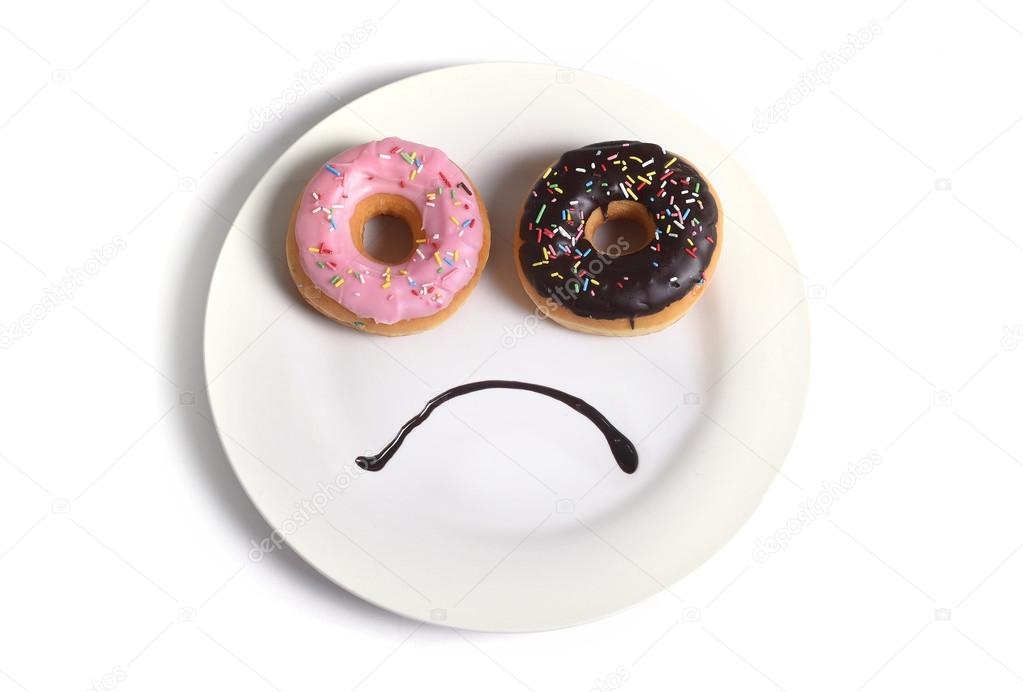 smiley sad face made on dish with donuts as eyes and chocolate syrup mouth in sugar sweet addiction diet and nutrition
