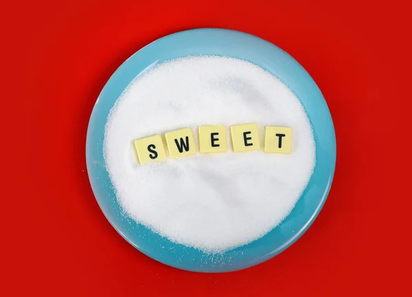 Palabra dulce letras de bloque en la cama de azúcar en plato azul sobre la estera roja en la adicción al azúcar — Foto de Stock