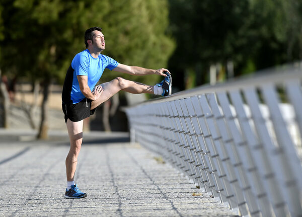 athlete man stretching legs warming up calf muscles before running workout leaning on railing city urban park
