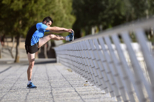 athlete man stretching legs warming up calf muscles before running workout leaning on railing city urban park