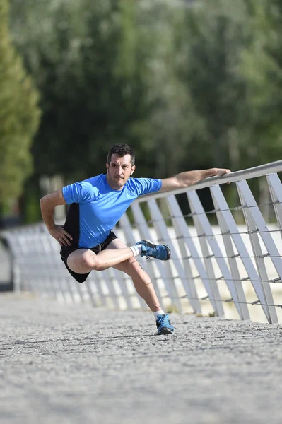 Sportler streckt Beine beim Aufwärmen der Muskeln vor dem Lauftraining, angelehnt an Geländer Stadtpark — Stockfoto