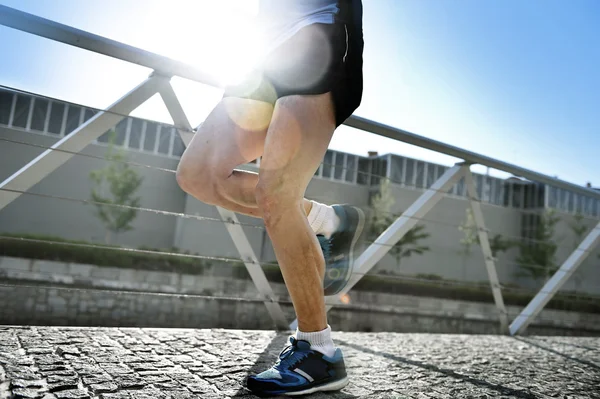 Cerrar las piernas y zapatos de hombre atlético joven practicando correr en el fondo urbano contraluz ascendente natural —  Fotos de Stock