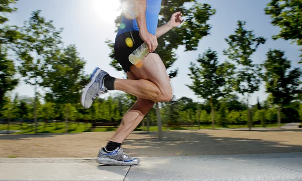 Крупним планом спортивні ноги молодого чоловіка, що бігає в міському парку з деревами на літній тренувальній сесії, практикуючи спорт здоровий спосіб життя концепції — стокове фото